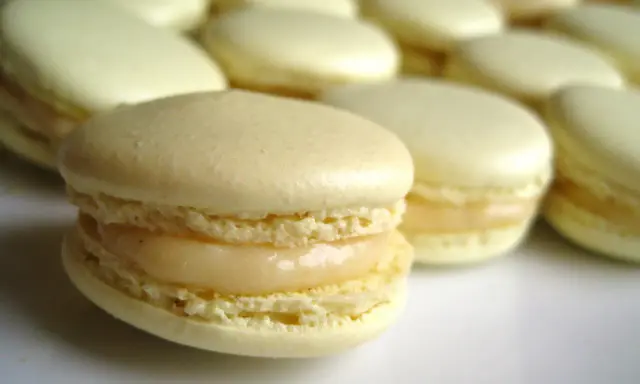 Un macaron meringue italienne, délicatement garni, se tient au premier plan, entouré d'autres douceurs pâles.