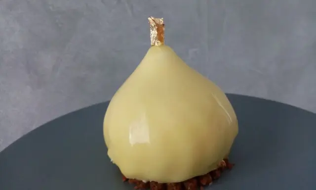 Délice en forme de poire, recouvert d'un glacage miroir jaune éclatant, sur un lit de crumble croquant, orné d'une touche de feuille d'or.