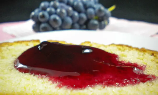 Tranche de gâteau moelleux nappée d'une généreuse gelée de raisin, avec une grappe de raisins bleus en arrière-plan.