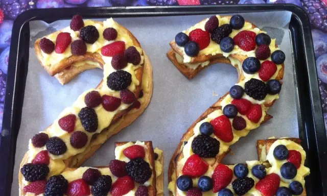 Un délicieux number cake aux fruits rouges, formant les chiffres 2 et 4, garni de crème pâtissière et de baies fraîches.