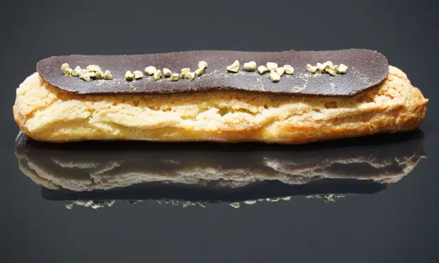 Un délicieux éclair au chocolat, garni de petits éclats dorés, repose sur une surface réfléchissante.