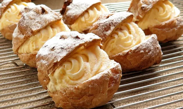 Pâte à choux au robot, garnies d'une crème onctueuse et saupoudrées de sucre glace, refroidissent sur une grille.