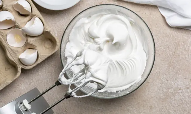 Meringue aérienne, blanc en neige, prête pour une recette gourmande. Des coquilles d'œufs vides à côté témoignent du travail.