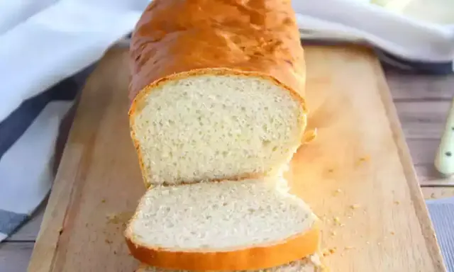 Un pain maison doré, tranché sur une planche en bois, parfait pour réussir son pain. La mie est aérée et la croûte appétissante.