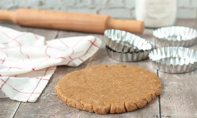 Pâte sablée prête pour la cuisson au four à chaleur tournante. Rouleau à pâtisserie, moules et torchon à proximité.