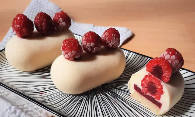 Entremets vanille-framboise sur assiette rayée, décorés de framboises fraîches.