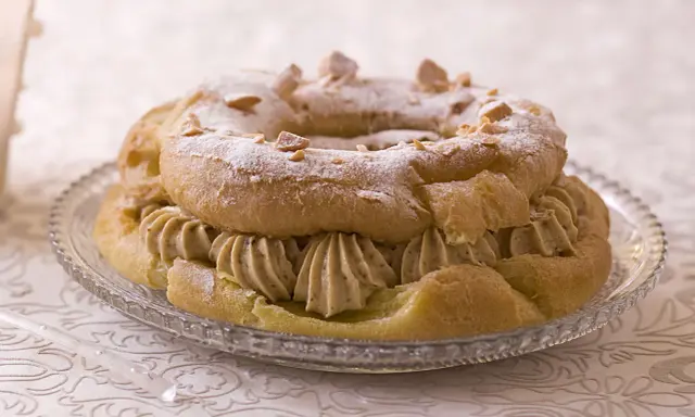 Bûche façon Paris-Brest, une couronne de pâte à choux garnie de crème onctueuse et saupoudrée de sucre glace et d'amandes effilées.