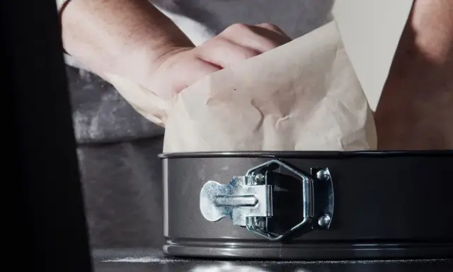 Mains expertes s'affairent à chemiser un moule avec du papier sulfurisé, préparant ainsi le terrain pour une future création culinaire.