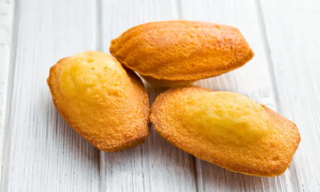 Trois madeleines dorées, parfaites pour la meilleure recette madeleine, sur un fond de bois clair.