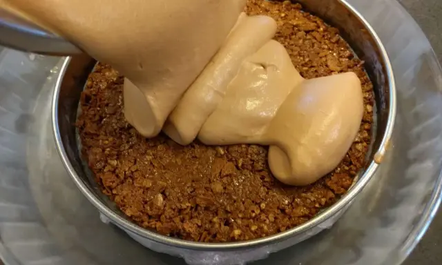 Une crème onctueuse est versée sur une base croustillante chocolat dans un moule.