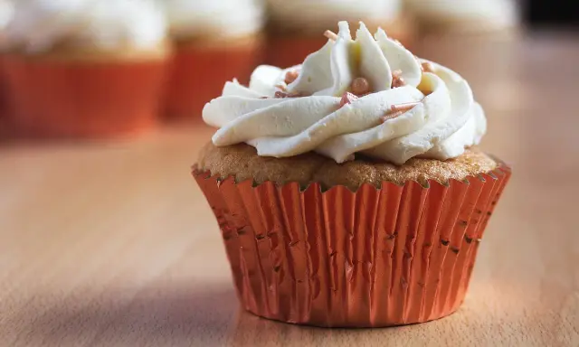 Un cupcake orné d'une généreuse ganache chocolat blanc, parsemé de perles rosées, dans un élégant caissette orange.