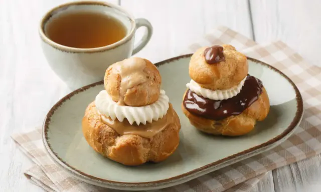 Deux religieuses au café, garnies de crème et nappées de chocolat ou de caramel, accompagnées d'une tasse de thé.