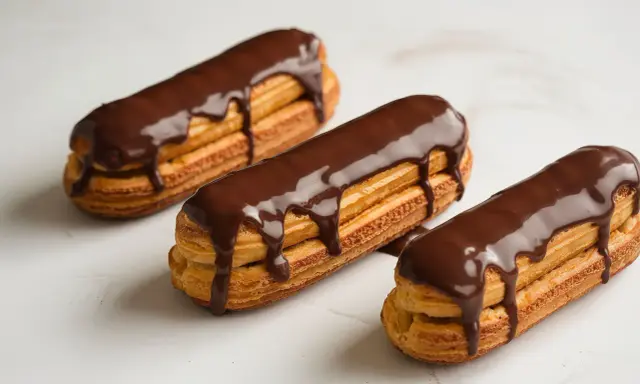 Trois éclairs au chocolat, parfaits pour une recette opera. La ganache dégouline sur la pâte à choux dorée.