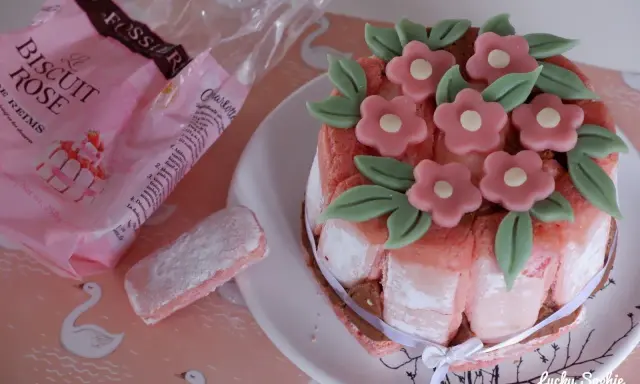 Charlotte aux biscuits roses de Reims, décorée de fleurs en pâte d'amande. Un biscuit rose saupoudré de sucre est à côté.