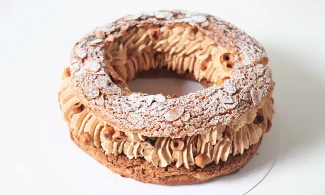 Un Paris Brest meilleur du chef, généreusement garni de crème pralinée et parsemé d'amandes effilées et de noisettes.