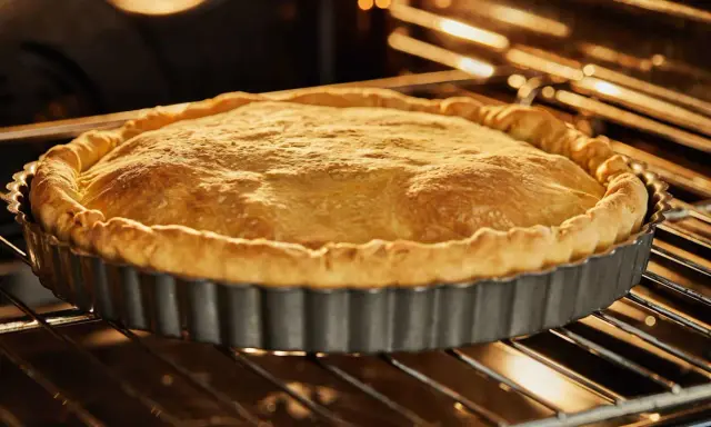 Tarte en cuisson à blanc dans son moule. La pâte brisée est dorée et gonflée, prête à être garnie.