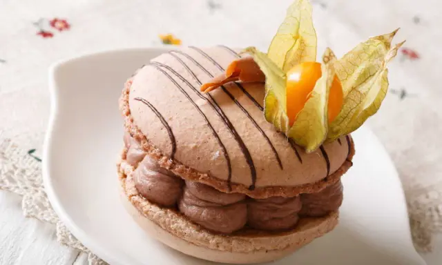 Un délicieux macaron chocolat au lait, garni de crème onctueuse et décoré d'une physalis orangée.