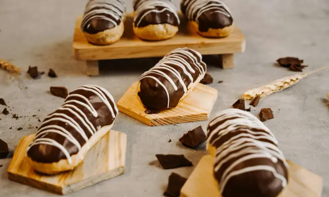 Éclairs gourmands avec un glaçage éclair chocolat brillant, décorés de fines rayures blanches. Des éclats de chocolat parsèment la table.