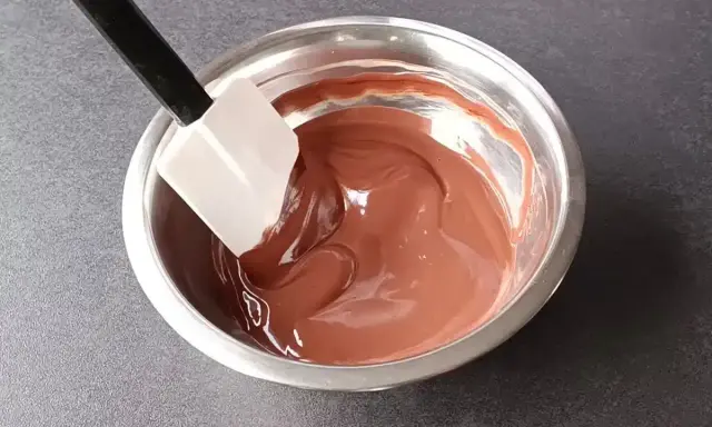 Spatule mélangeant une ganache au chocolat noir onctueuse dans un bol en métal.