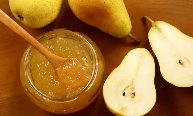 Un pot de confiture de poires maison, avec une cuillère en bois, entouré de poires fraîches coupées et entières sur fond de bois.
