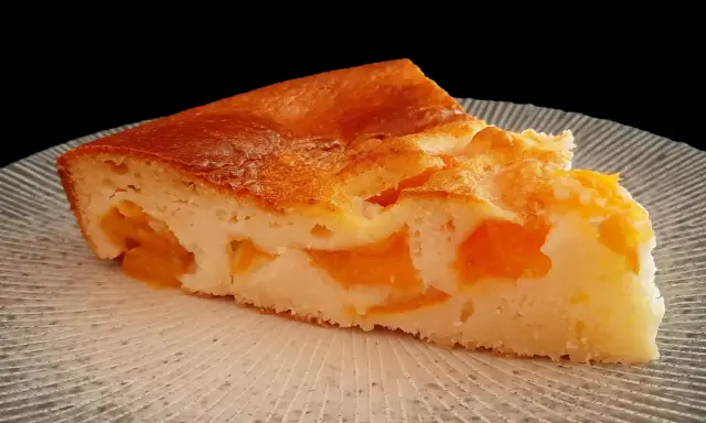 Tranche de clafoutis abricot, une création de chef, sur une assiette texturée.