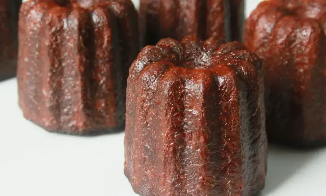 Plusieurs cannelés dorés, tout juste sortis du four, prêts pour la dégustation. La cuisson des cannelés révèle leur croûte caramélisée.