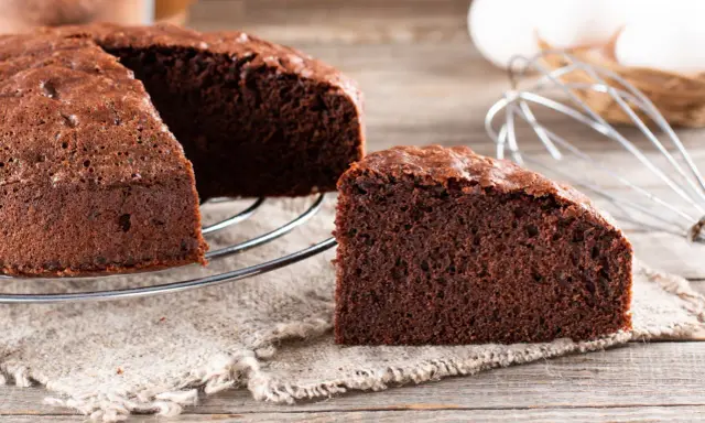Un délicieux gâteau génoise chocolat, moelleux et aéré, prêt à être dégusté. Des ingrédients frais comme des œufs et du cacao sont visibles en arrière-plan.