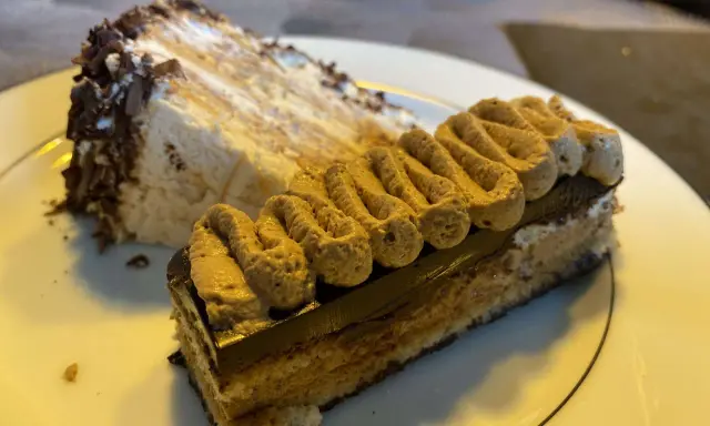 Deux parts de gâteau, dont une avec une crème légère et des copeaux de chocolat, l'autre un opéra conticini, sur une assiette blanche.