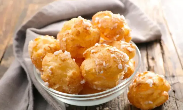 Un bol de chouquettes maison dorées et saupoudrées de sucre perlé, posé sur une table en bois.