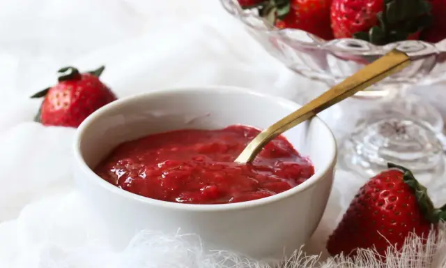 Un bol de compotée de fraise pour gâteau, prêt à être dégusté. Des fraises fraîches sont disposées autour.