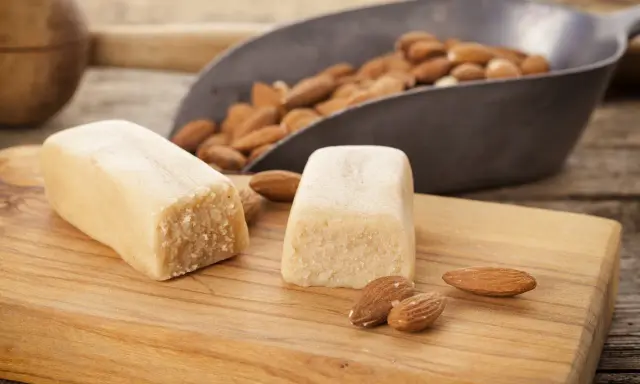Deux blocs de pâte d'amande et des amandes dans une pelle, prêts pour une recette de pâte d'amande maison.