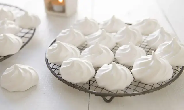 Douces meringues blanches, prêtes pour la cuisson. Elles reposent sur des grilles, évoquant la douceur et la légèreté.