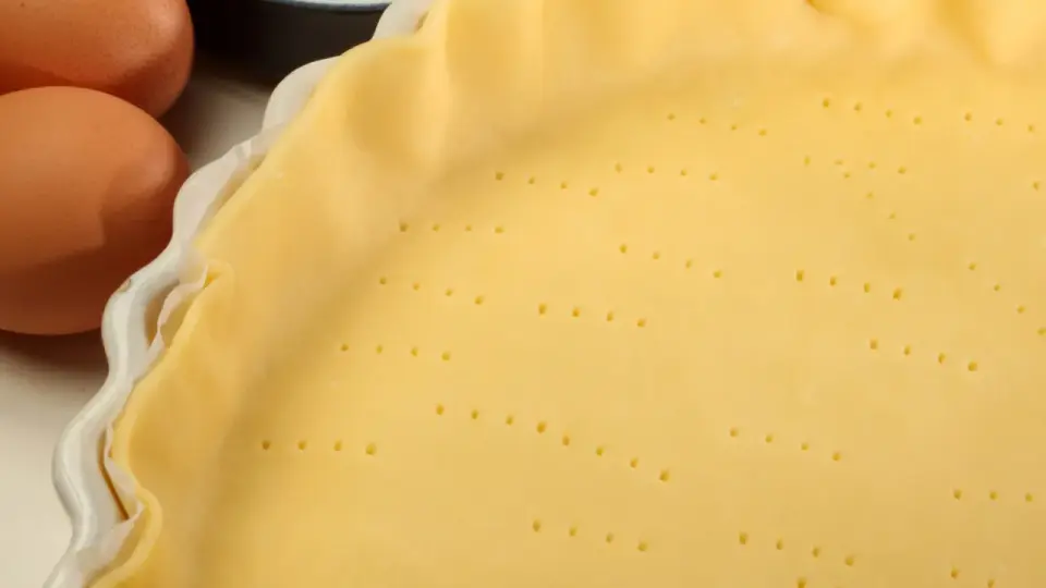 Pâte feuilletée prête pour la cuisson au four, avec des œufs et de la farine en arrière-plan.