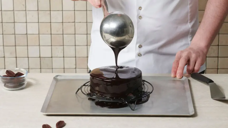 Un chef verse un glaçage chocolat au lait onctueux sur un gâteau rond.