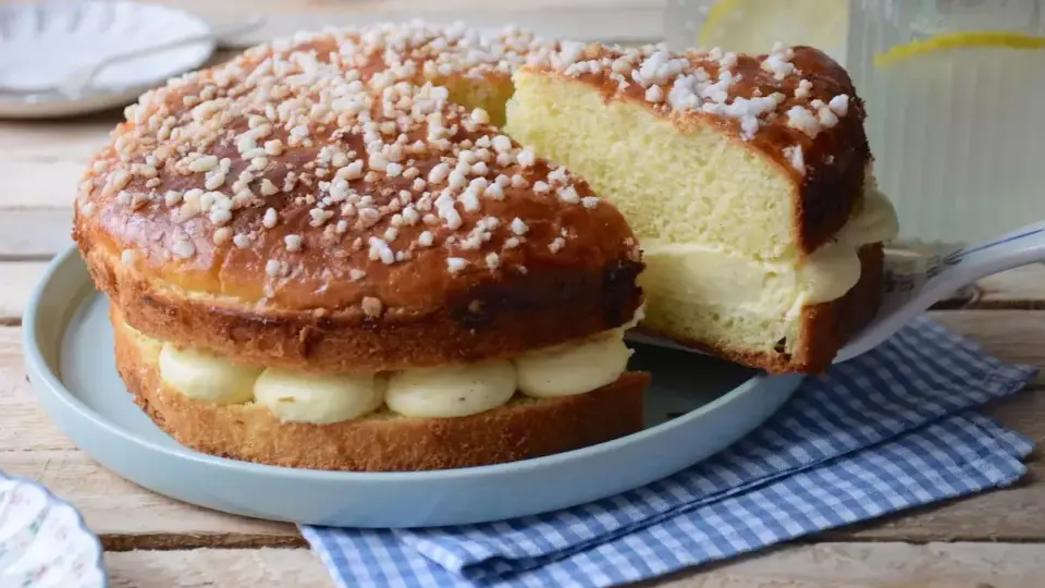 Un délicieux gâteau tropézien, garni de crème onctueuse et saupoudré de sucre perlé. Une part est servie sur une pelle à gâteau.