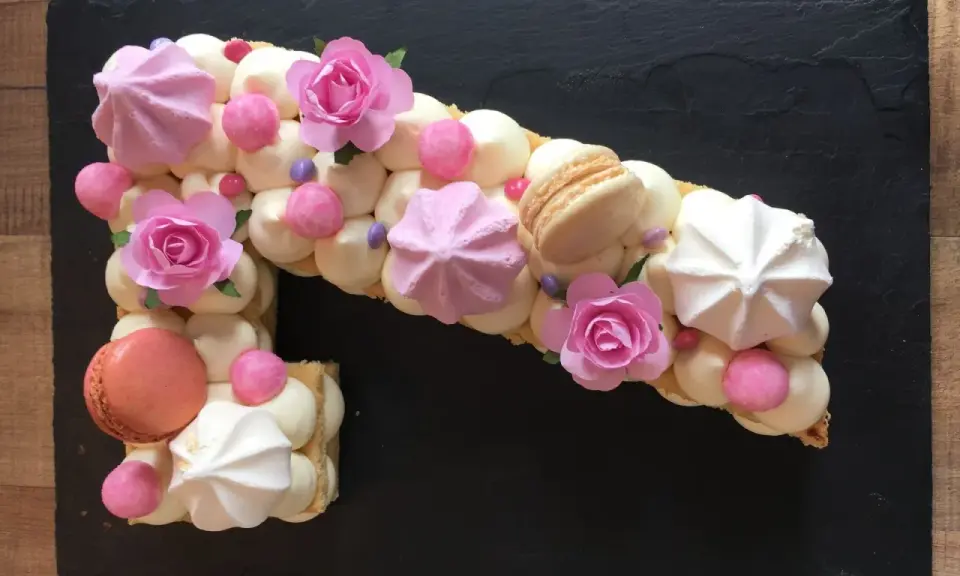 Un biscuit joconde number cake en forme de 1, décoré de crème, meringues, macarons et roses en sucre.
