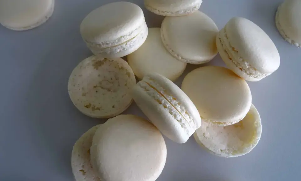 Des macarons blancs, certains assemblés, d'autres séparés, prêts pour la cuisson macaron chaleur tournante.