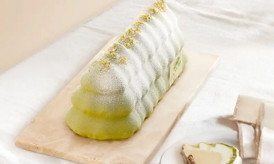 Bûche glacée verte, saupoudrée de sucre glace et de paillettes dorées, évoquant un biscuit madeleine.