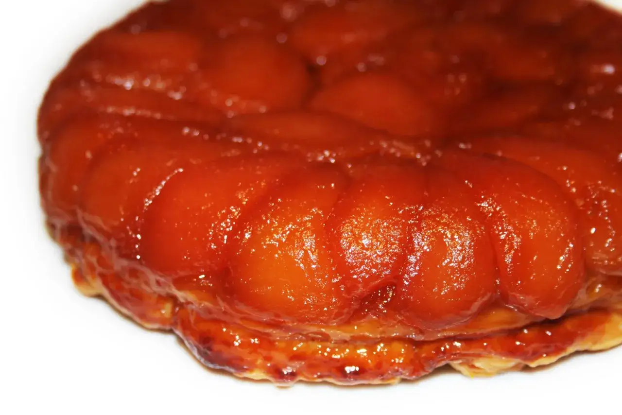 Gros plan sur une délicieuse tarte tatin aux pommes caramélisées, sa pâte dorée et ses fruits brillants invitent à la dégustation.