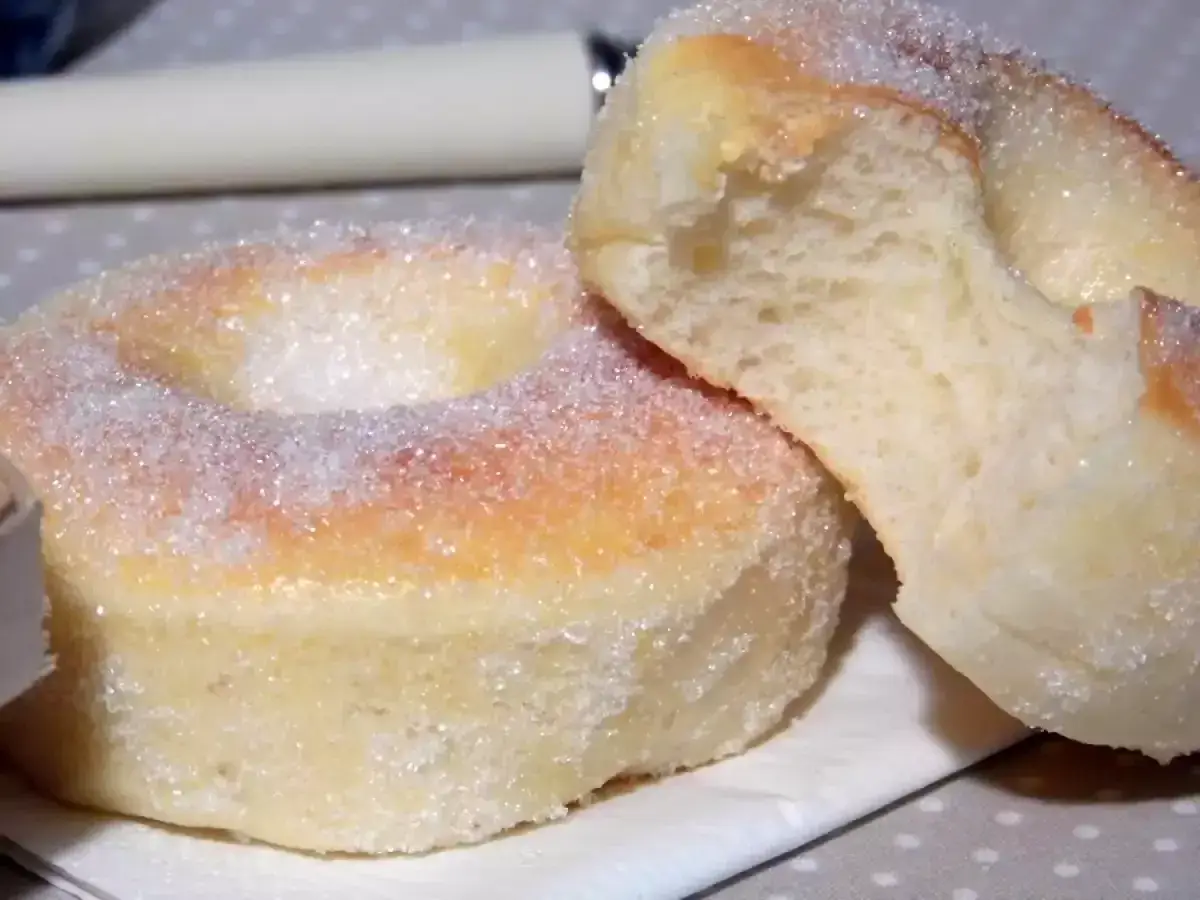 Deux beignets au four, saupoudrés de sucre, dont l'un est coupé, révélant une mie moelleuse.