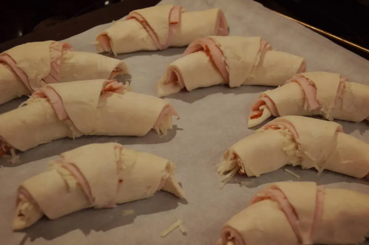 Huit croissants garnis de jambon et de fromage, prêts à être cuits. Une délicieuse pâte à pâte pour un en-cas savoureux.