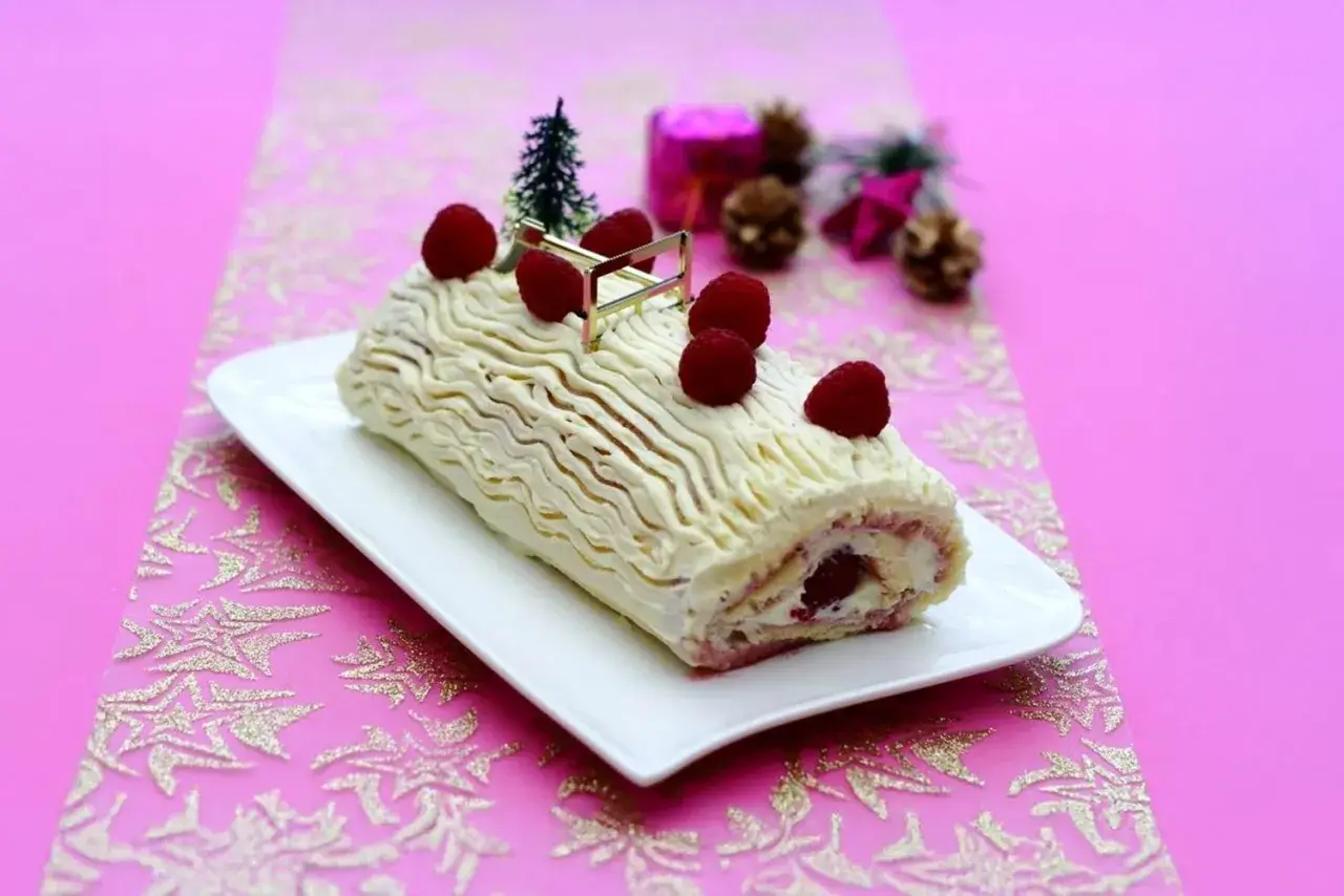 Bûche de Noël au chocolat blanc et framboise, décorée de fruits rouges et d'un petit sapin. Une délicieuse recette pour les fêtes.