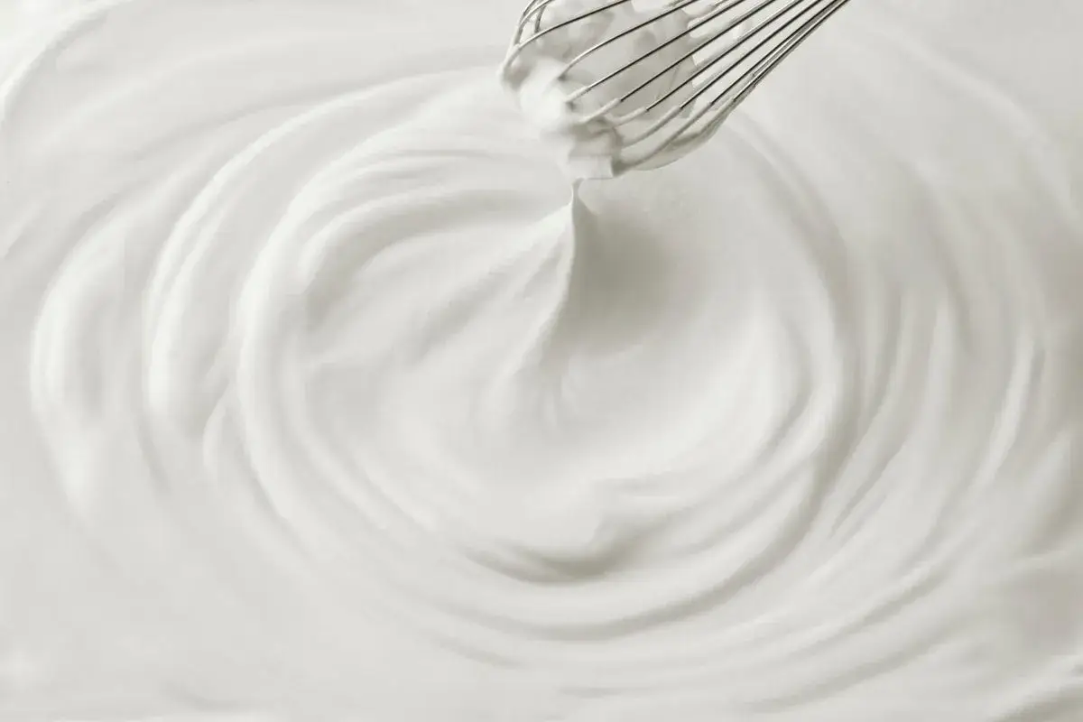Un fouet mélangeant une crème chantilly aérienne, créant des tourbillons doux et onctueux.