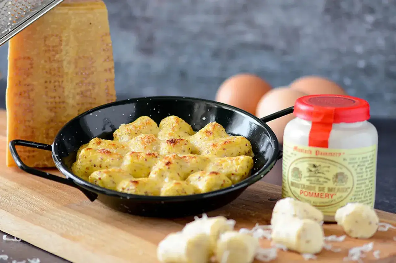 Gnocchi à la parisienne gratinés, servis dans une poêle avec du fromage râpé, des œufs et de la moutarde de Meaux.