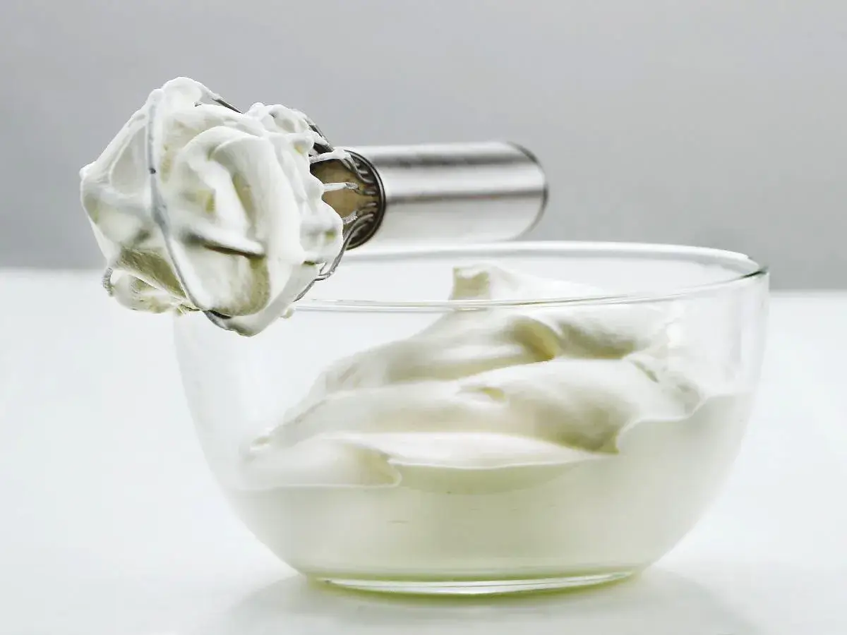 Crème fouettée aérienne prête à garnir un gâteau, dans un bol en verre.