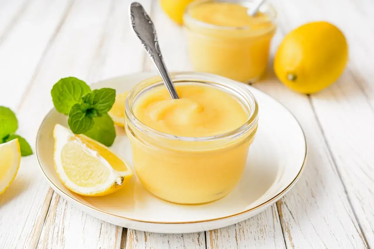 Un pot de crème citron onctueuse, garni de menthe fraîche et de quartiers de citron, prêt à être dégusté.