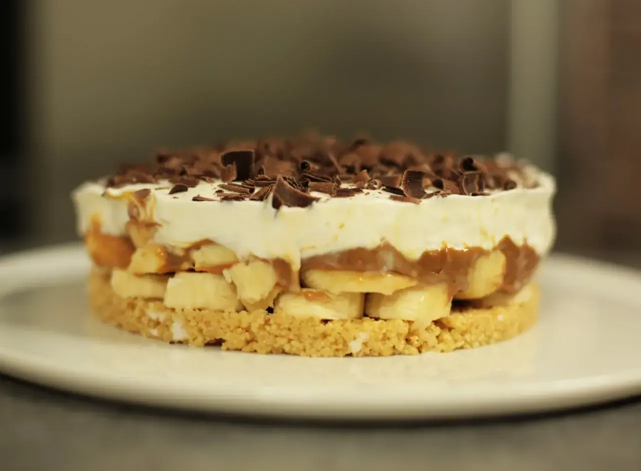 Gâteau banoffee traditionnel : une base biscuitée, des rondelles de banane, une sauce caramel onctueuse, de la crème fouettée et des copeaux de chocolat.
