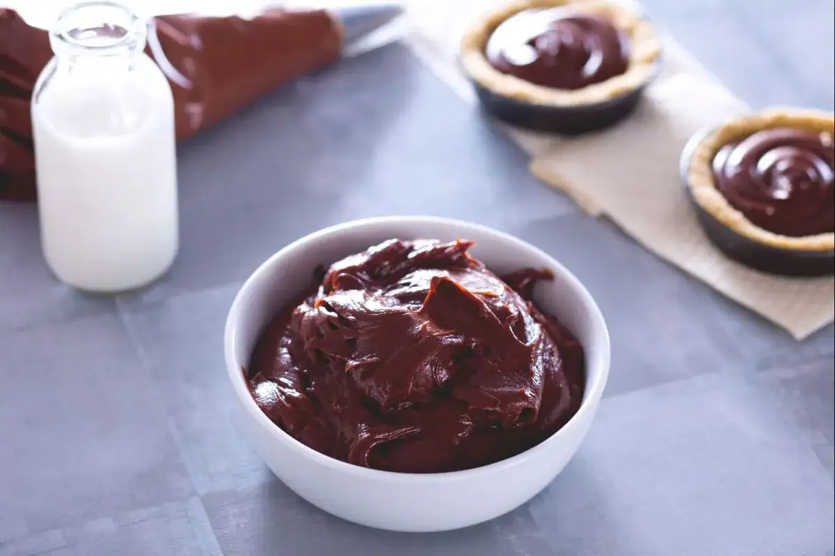 Un bol de ganache chocolat au lait onctueuse, pr&ecirc;t &agrave; garnir des tartelettes. Une bouteille de lait et une poche &agrave; douille compl&egrave;tent la sc&egrave;ne.