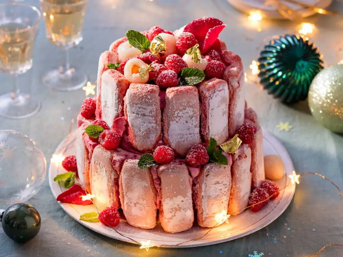 Magnifique Charlotte aux biscuits roses, garnie de framboises, litchis et feuilles de menthe, prête pour une fête festive.
