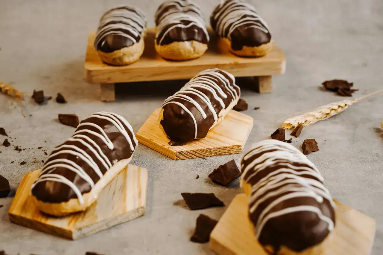&Eacute;clairs gourmands avec un gla&ccedil;age &eacute;clair chocolat brillant, d&eacute;cor&eacute;s de fines rayures blanches. Quelques morceaux de chocolat et une &eacute;pi de bl&eacute; compl&egrave;tent la sc&egrave;ne.